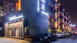 A hotel with a prominent illuminated sign, a modern facade, and a parking area with several cars. - Qiuguo Hotel Beijing by Bayluxury (Beijing)