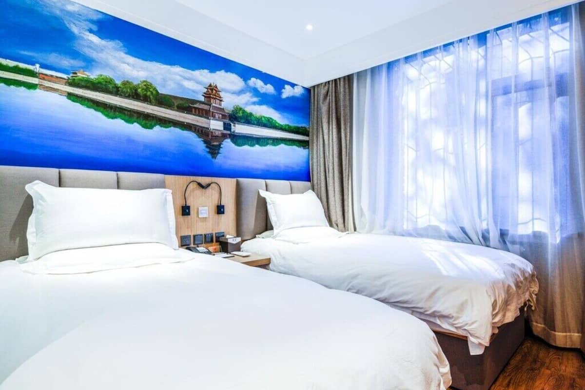 Una habitació d'hotel amb dos llits, un mural gran d'un paisatge, i vista a un conjunt d'aigua a través de cortines translúcides.
