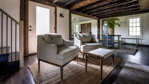 A spacious room with a high ceiling, wooden beams, a large window, and a dining area with a table and chairs. - The Farmhouse Stay (Haddam)