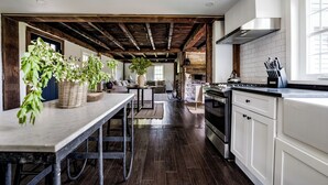 A modern kitchen with dark wooden floors, white cabinetry, and a large island. - The Farmhouse Stay (Haddam)