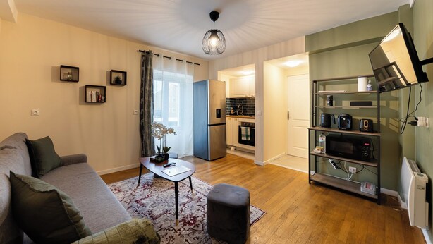A compact living space with a sofa, a small table, a decorative plant, a kitchen area with a refrigerator, oven, and microwave, and a shelf with kitchen items. - Green Dream: proximity Paris & Disneyland (Villiers-sur-Marne)