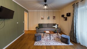 A living room with a grey sofa, a coffee table, two ottomans, a patterned rug, and a ceiling light fixture. - Green Dream: proximity Paris & Disneyland (Villiers-sur-Marne)