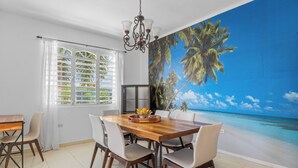 A dining area with a wooden table and chairs, a chandelier, and a large mural of a beach scene.