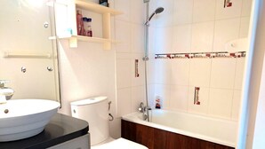 A bathroom with a white toilet, a sink, and a bathtub. There are shelves above the sink and a showerhead above the bathtub. - Sea view cool apartment with a balcony (Le Barcarès)