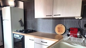 A compact kitchen with a stove, oven, and sink. There is a wooden cutting board and a red appliance on the counter. - Sea view cool apartment with a balcony (Le Barcarès)