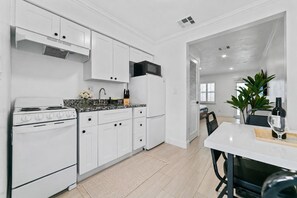 A modern kitchen with white cabinetry, a stove, and a microwave. There is a dining area with a table and chairs. - Modern 1BR Apartment - King Bed & Central (Lauderdale-by-the-Sea)