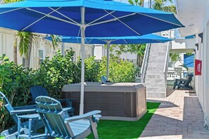 An outdoor patio area with a hot tub, lounge chairs, and a blue umbrella providing shade. - Modern 1BR Apartment - King Bed & Central (Lauderdale-by-the-Sea)