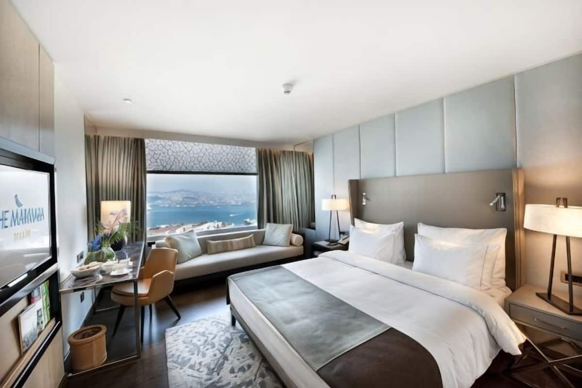 A hotel room with a bed, a desk, a TV, and a view of the city.