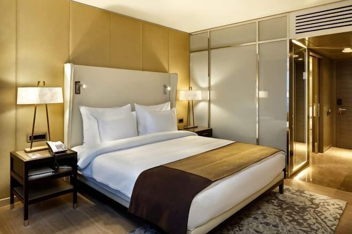 A hotel room with a large bed, bedside lamps, a telephone, a wardrobe, and a door leading to a bathroom.