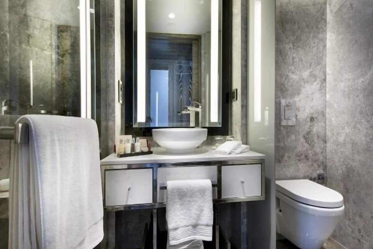 A modern bathroom with a large mirror, a white sink, a toilet, and a towel rack.