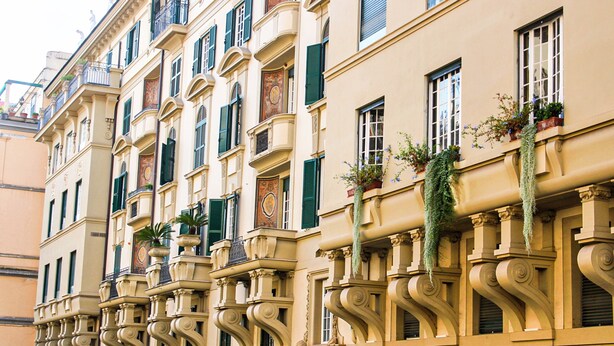 Ein Gebäude mit mehreren Balkonen, grünen Fensterläden und dekorativen Stuckelementen.