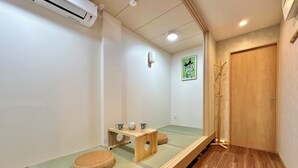 A traditional Japanese room with tatami flooring, a wooden table with cups and a teapot, a wooden coat rack, and a sliding door.