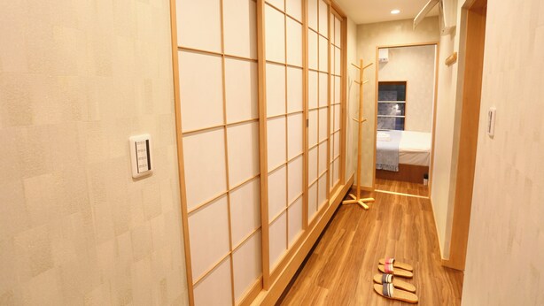 A hallway with sliding doors, a bed with a checkered blanket, and a wooden floor.