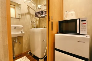 A compact hotel bathroom with a sink, a compact washing machine, and a microwave.