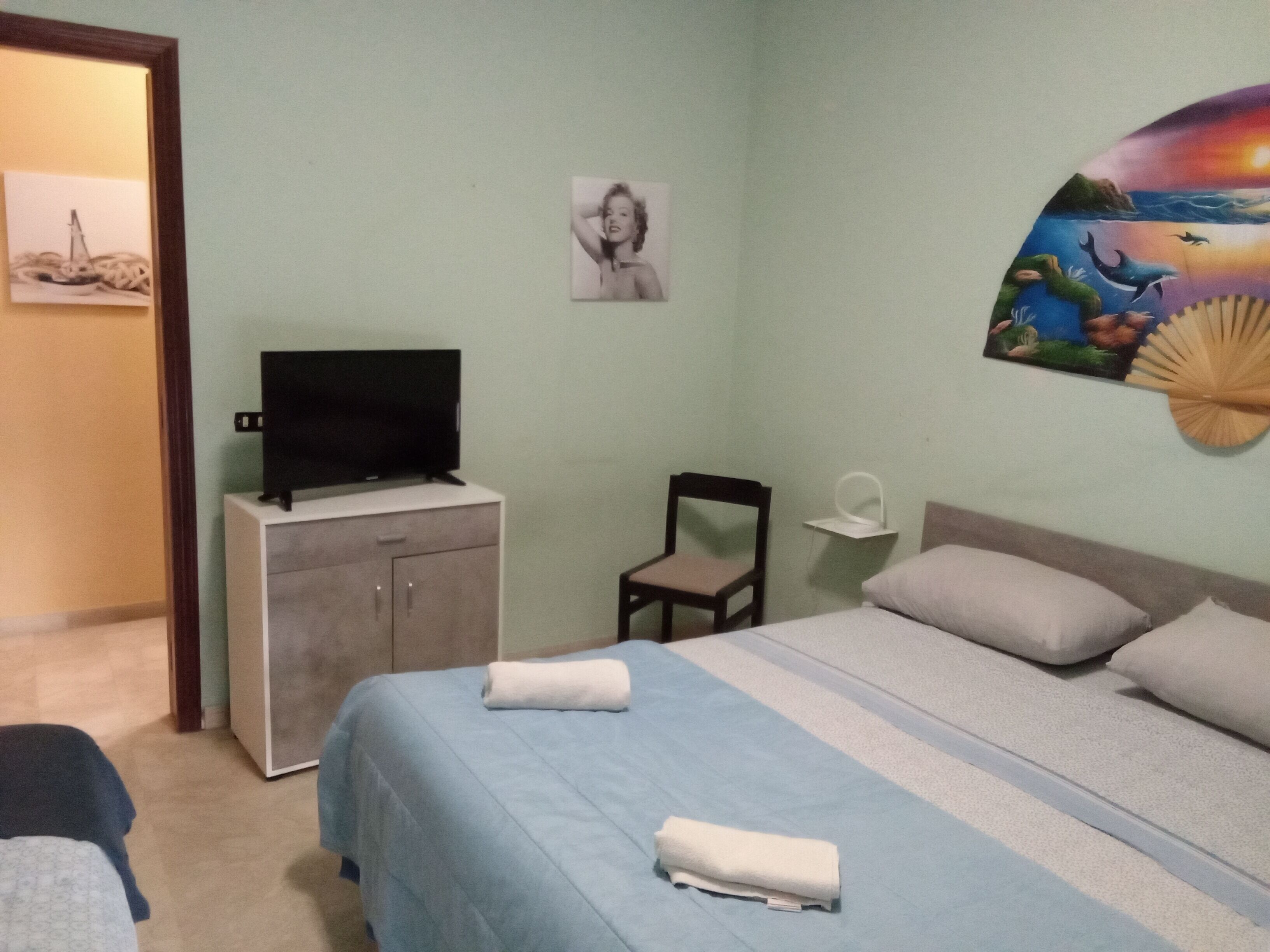 Ein Schlafzimmer mit einem Bett, einem Fernseher auf einem Schrank, einem Sessel und einer Wand mit einem Gemälde.