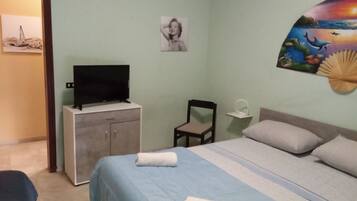 Ein Schlafzimmer mit einem Bett, einem Fernseher auf einem Schrank, einem Sessel und einer Wand mit einem Gemälde.