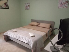 A bedroom with a bed, pillows, a TV, and a small table.