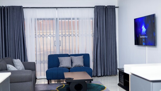 A modern living room with a grey sofa, a blue sofa, a coffee table, and a TV mounted on the wall. - Tranquil, Secure Haven in the Heart of Harare. (Harare)