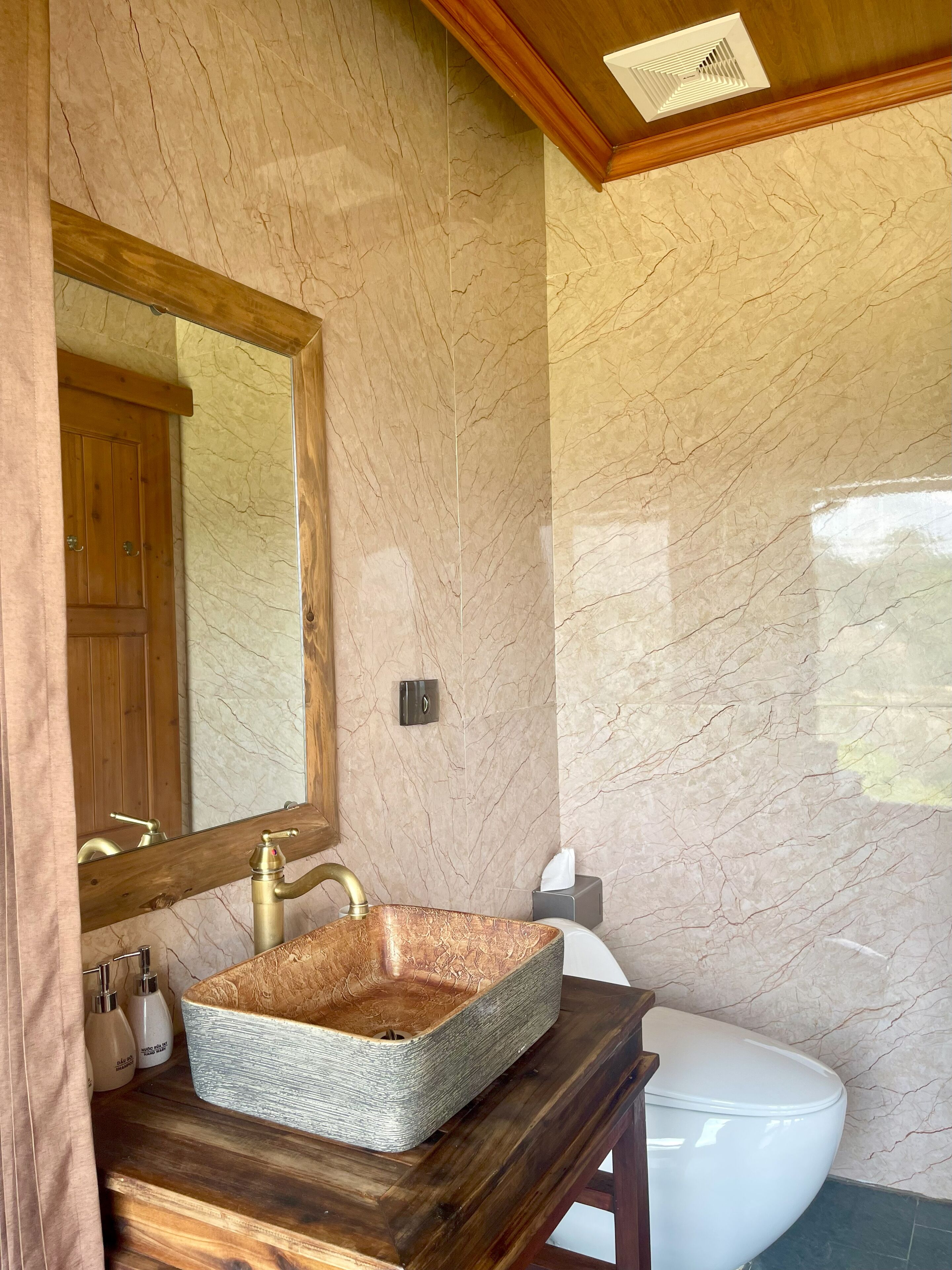 Une salle de bain avec un mur en marbre, un meuble-lavabo en bois, un grand miroir et des toilettes blanches.