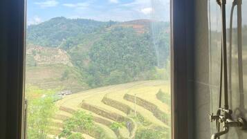 Un baño con ducha, una ventana con vistas a campos escalonados y colinas.