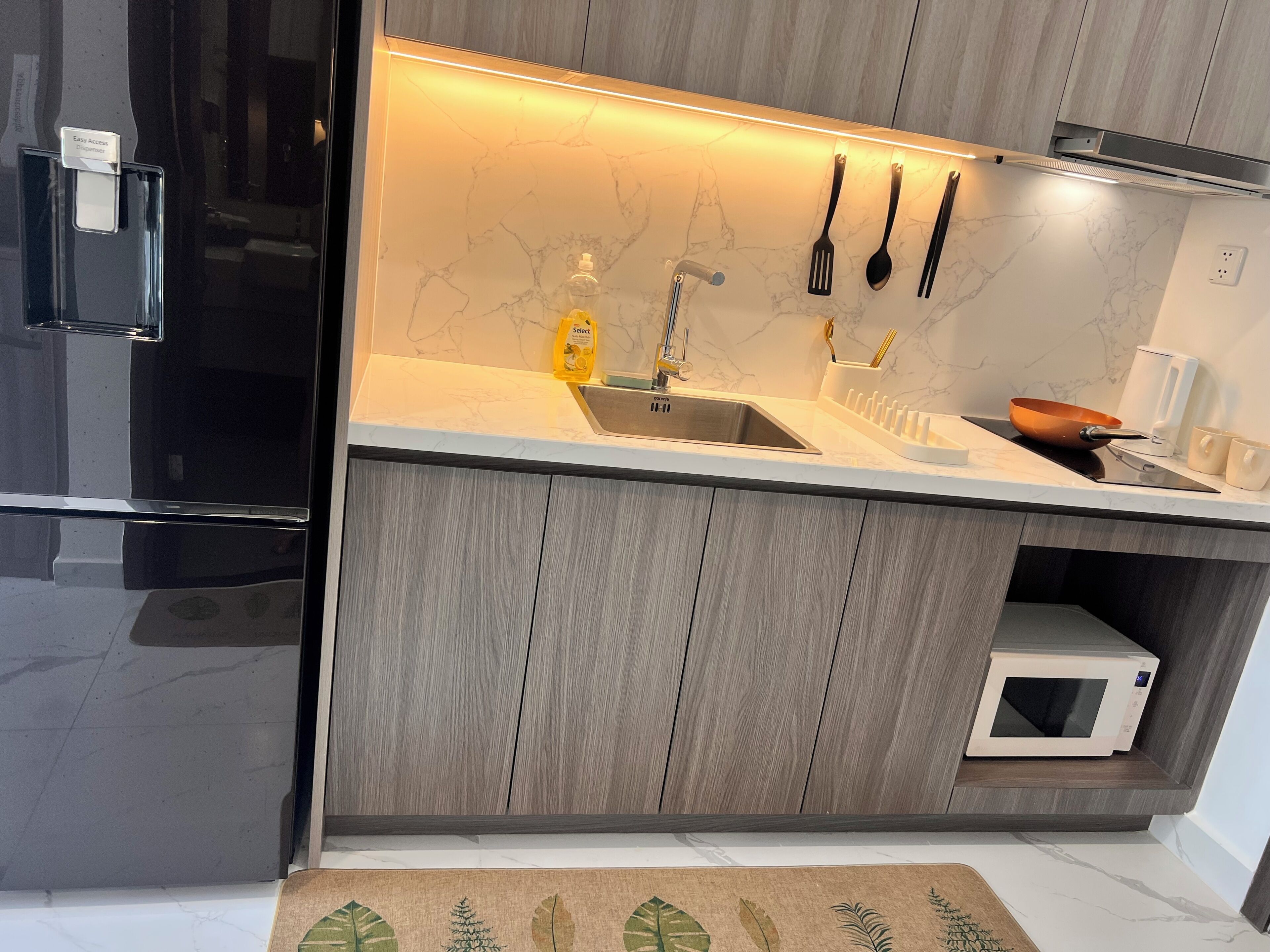 A modern kitchen with a built-in microwave, stainless steel sink, and wooden cabinets.