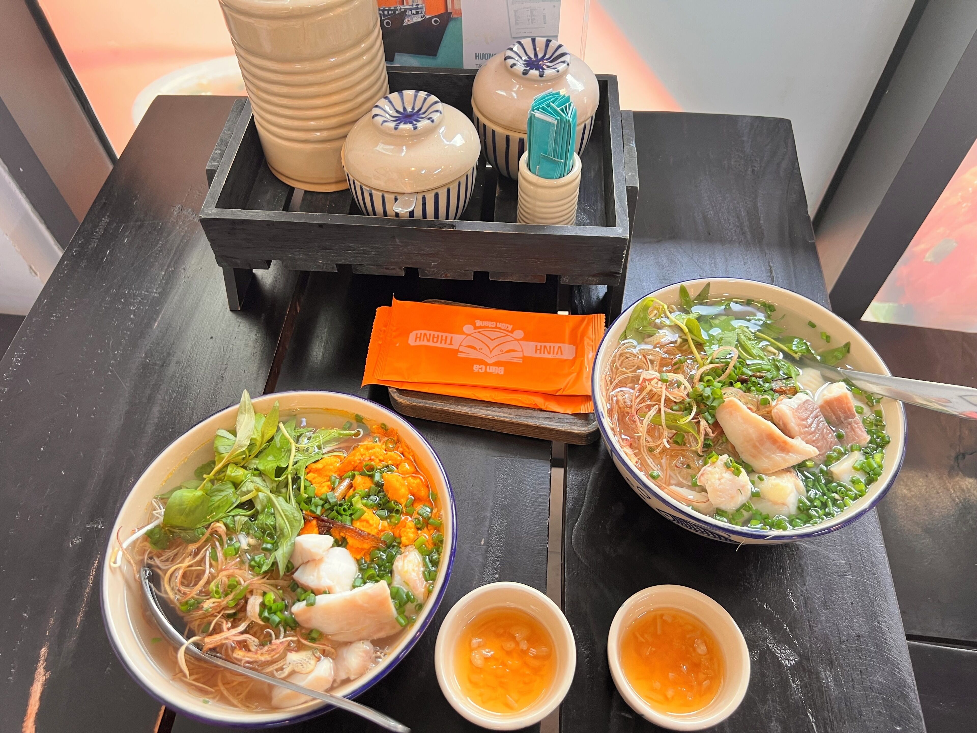 Une table avec deux bols de soupe aux nouilles, un plateau avec des objets décoratifs et un petit paquet orange.