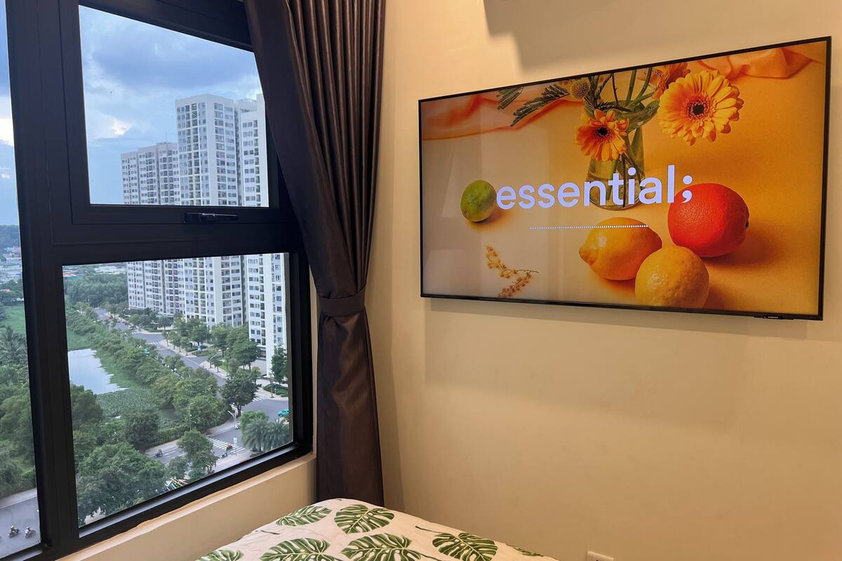 Une chambre d’hôtel avec un lit, une fenêtre avec des rideaux et un téléviseur fixé au mur qui affiche une image de fruits et de fleurs.