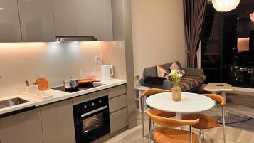 A modern kitchen with an oven, a dining area with a round table and chairs, and a living area with a sofa and a view of the city.