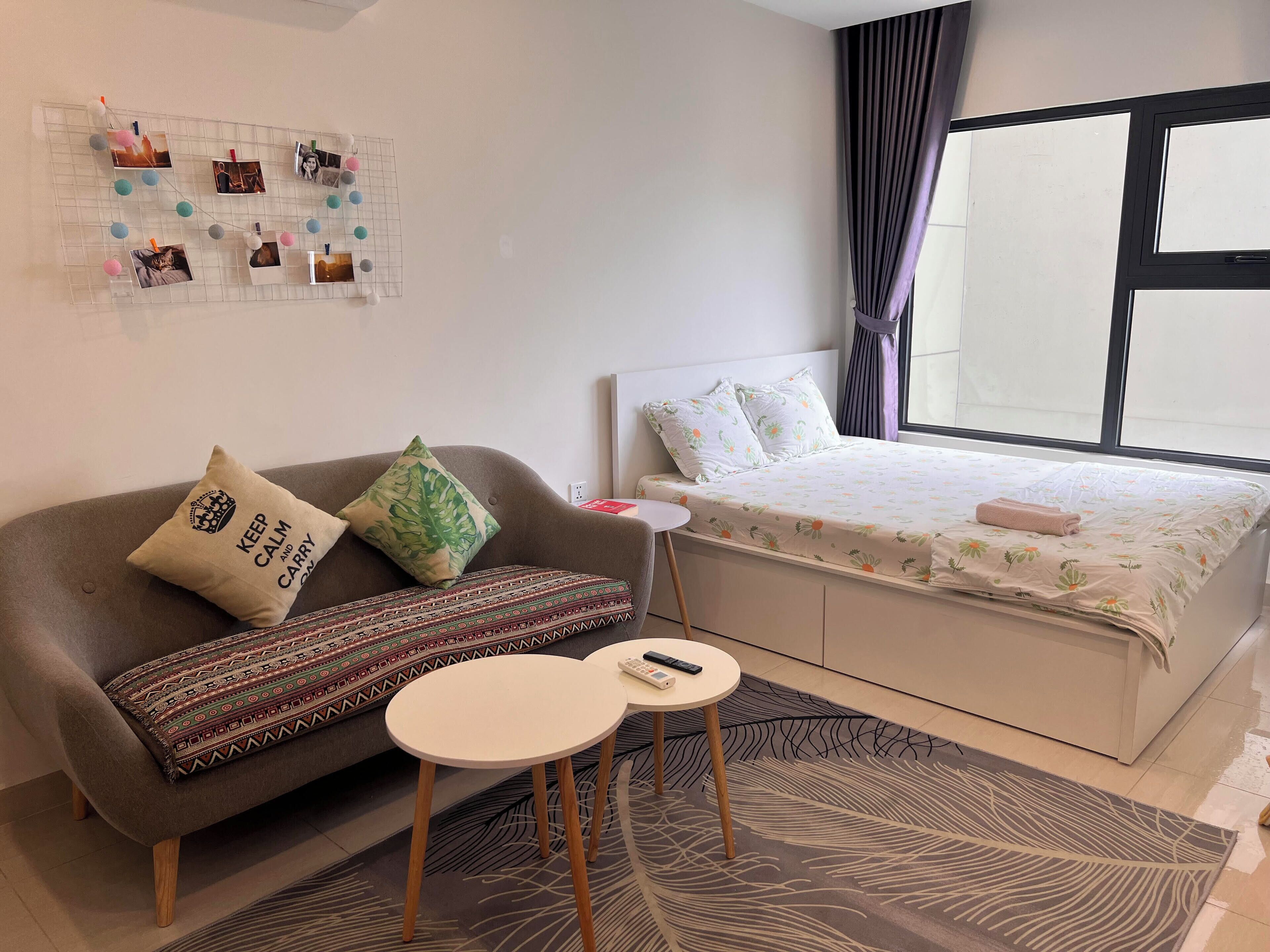 Mukava hotellihuone, jossa on sänky, sohva, pieni pöytä ja seinälle kiinnitetty valokuvien esillepano.
