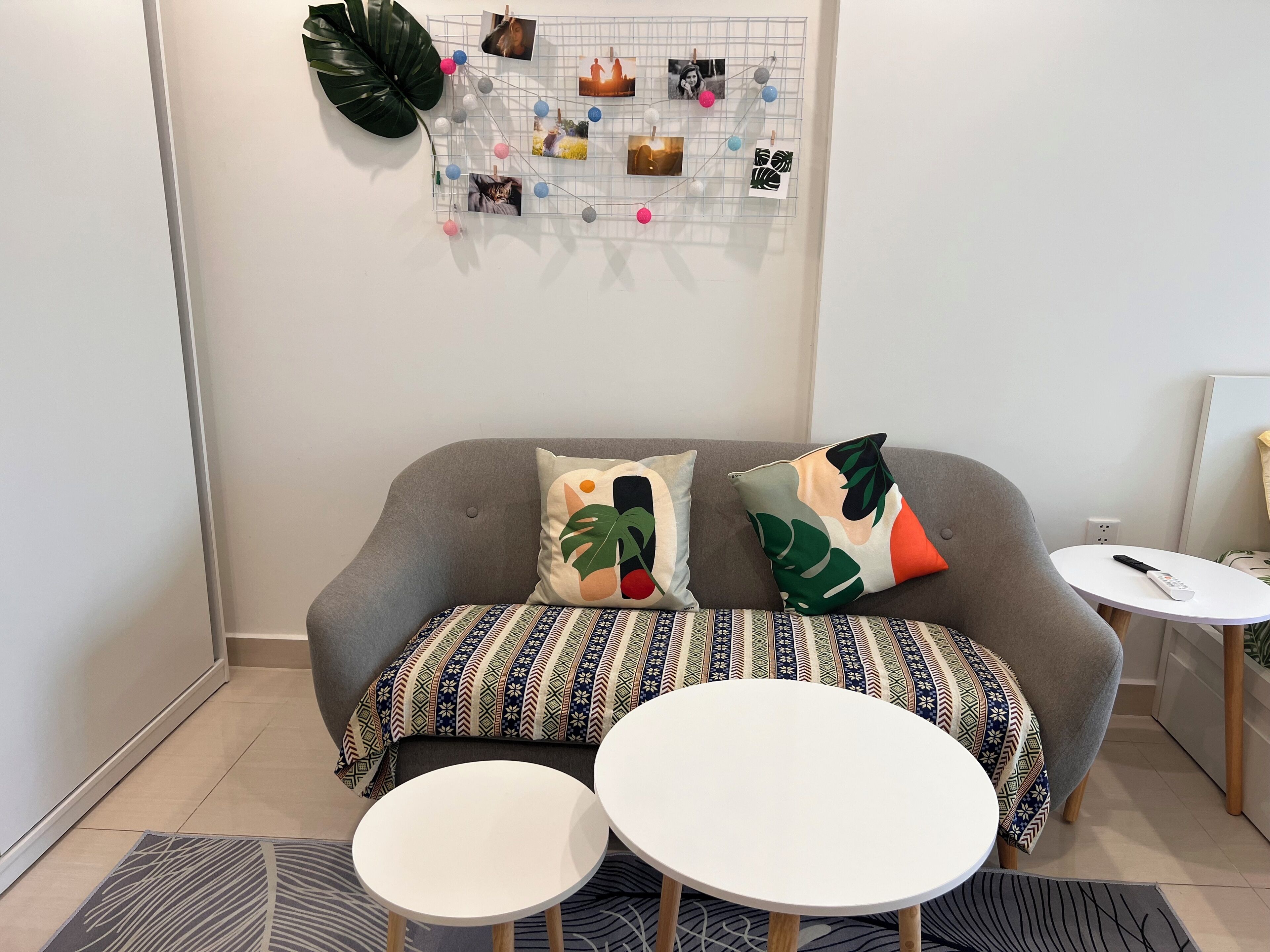A living room with a grey sofa, patterned cushions, a wall-mounted photo collage, and two round tables.