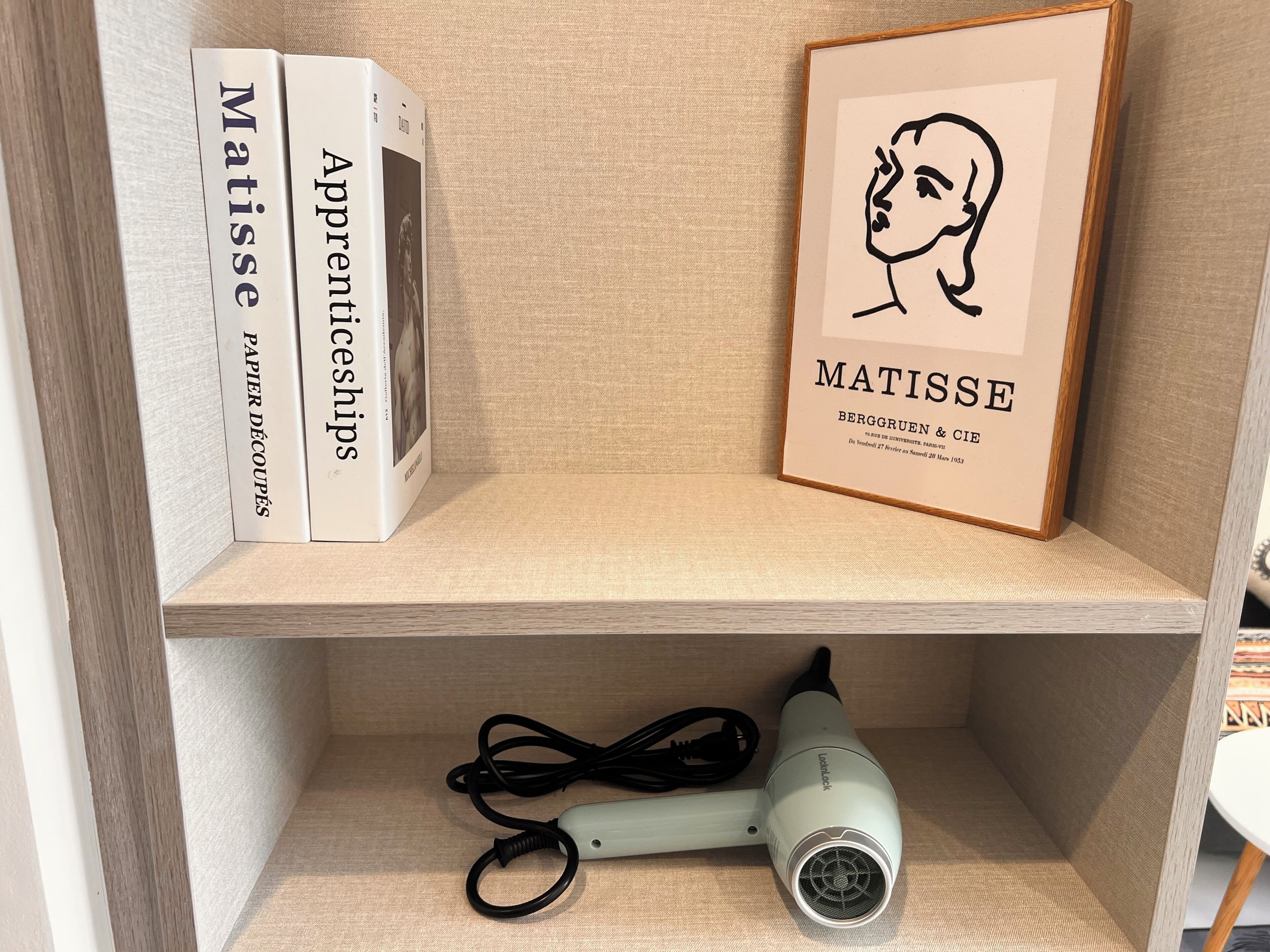Una estantería con una obra enmarcada, un libro y un secador de pelo.
