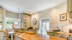 A kitchen with a wooden countertop, white cabinets, a clock, and a window overlooking a garden.