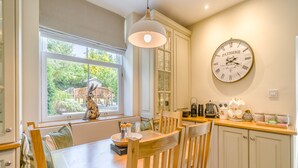 A dining area with a wooden table, chairs, a clock, and a window with a view of greenery.