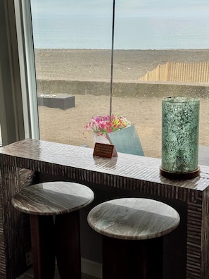 A view from a window with a beach in the background, a vase with flowers, and a green textured object on a table.