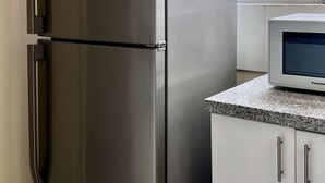 Un réfrigérateur en acier inoxydable doté d’un compartiment congélateur, un four à micro-ondes posé sur un plan de travail en granit, et des meubles de cuisine blancs avec des poignées argentées.