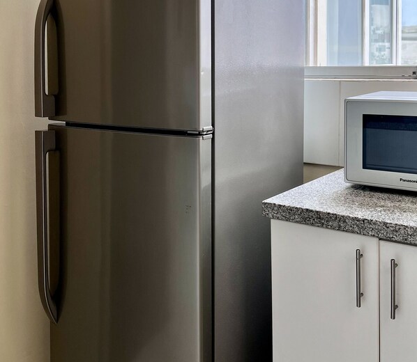 A stainless steel refrigerator with a freezer compartment, a microwave on a granite countertop, and white cabinets with silver handles. - A comfortable apartment, a great location, and a warm atmosphere for your stay🌊✨Escape to Lima as a couple! (Miraflores)