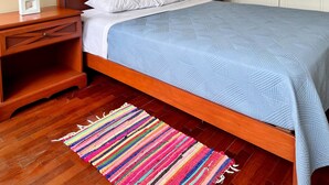 Un lit bien fait, avec une couette bleue, une tête de lit en bois, des tables de chevet avec des lampes et un tapis rayé et coloré sur un plancher en bois.