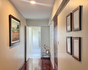 A hallway with framed artwork on the walls, a wooden floor, and a door leading to another room. - A comfortable apartment, a great location, and a warm atmosphere for your stay🌊✨Escape to Lima as a couple! (Miraflores)