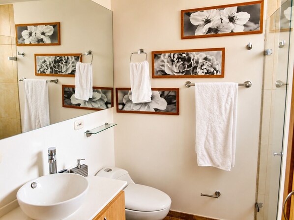 A bathroom with a large mirror, a sink, a toilet, and multiple framed floral pictures on the wall.