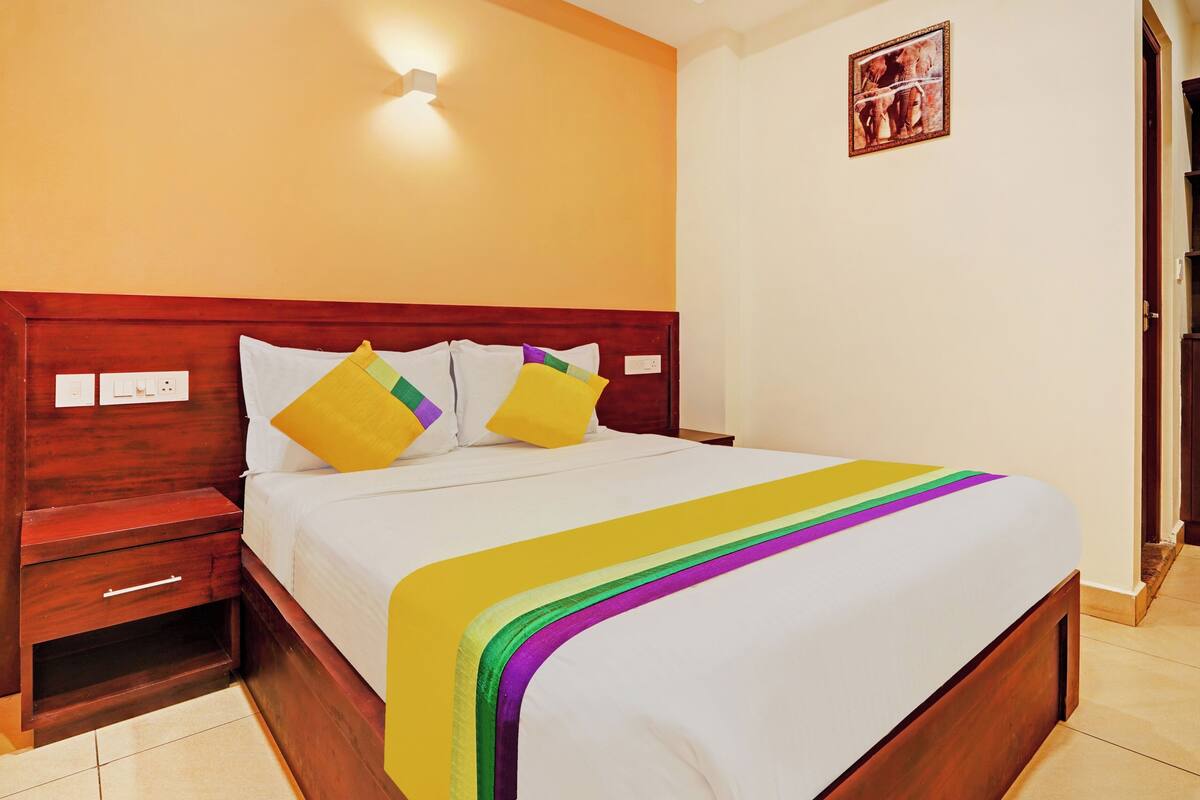 A neatly made bed with a wooden headboard, a bedside table with a drawer, and a wall-mounted light fixture.