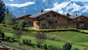 A chalet-style building with a sloped roof, surrounded by a well-maintained lawn and a mountain backdrop. - Chalet RoyAlp Hotel and Spa (Ollon)