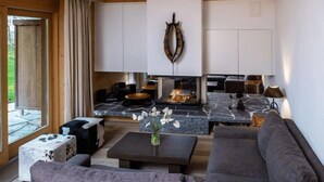 A modern living room with a stone fireplace, a sofa, a coffee table, and a view of the outdoors. - Chalet RoyAlp Hotel and Spa (Ollon)