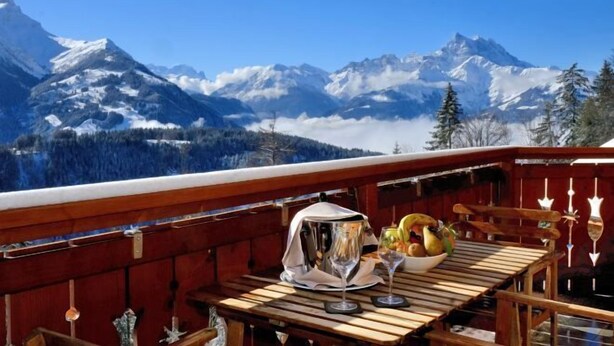 A wooden deck with a table set for dining, overlooking snow-capped mountains. - Chalet RoyAlp Hotel and Spa (Ollon)