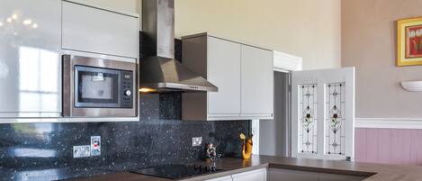 A modern kitchen with stainless steel appliances, a black granite countertop, and a recessed cooktop.