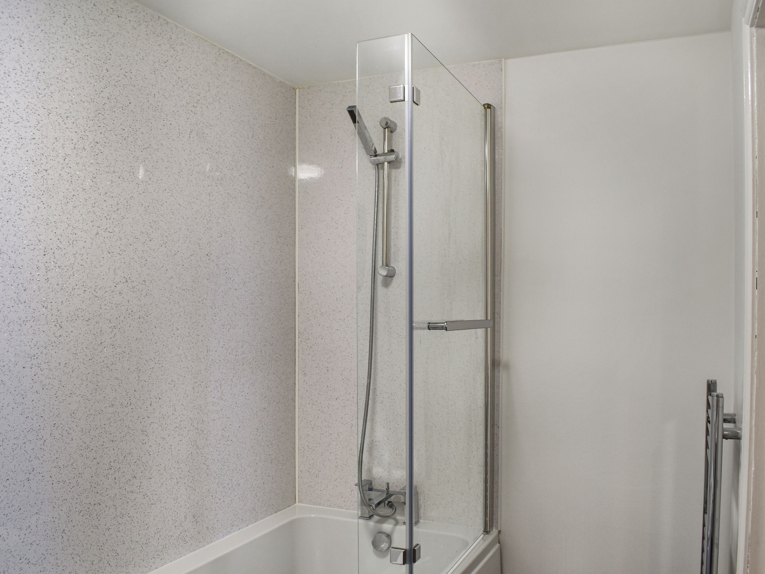 A glass-enclosed shower with a handheld showerhead and a handheld faucet.