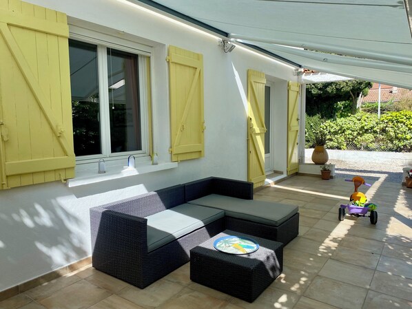 A covered patio area with a sectional sofa, a small table, and a child's toy car.