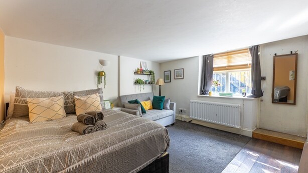 A bedroom with a bed, a sofa, a window with curtains, a radiator, and a mirror. - Cozy Flat in the Heart of Camden (Greater London)