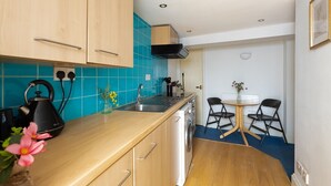 A compact kitchen with wooden cabinets, a sink, and a small dining area with two chairs and a table. - Cozy Flat in the Heart of Camden (Greater London)