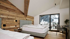 Ein modernes Schlafzimmer mit Holzboden, einem großen Bett mit weißer Bettwäsche, einem Schreibtisch mit Stuhl und Blick auf einen verschneiten Berg.