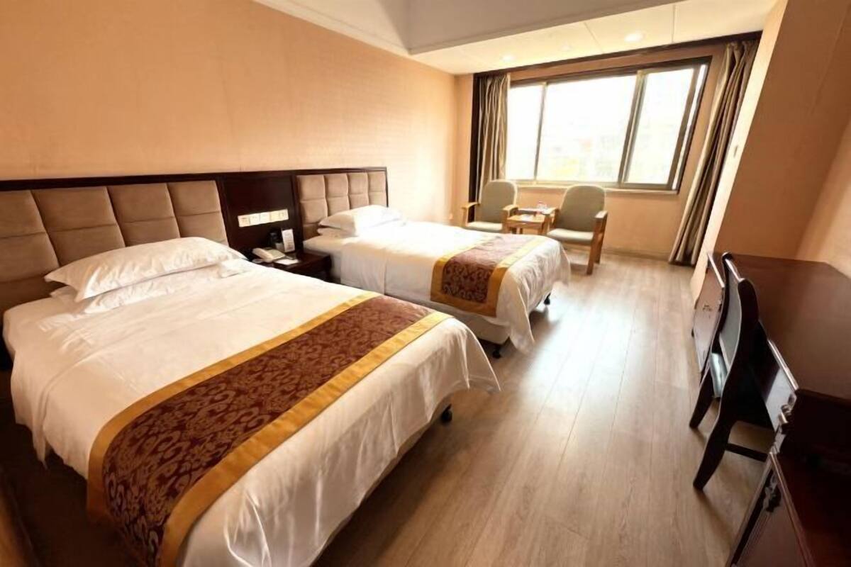 A hotel room with two beds, a desk, a chair, and a window with curtains.